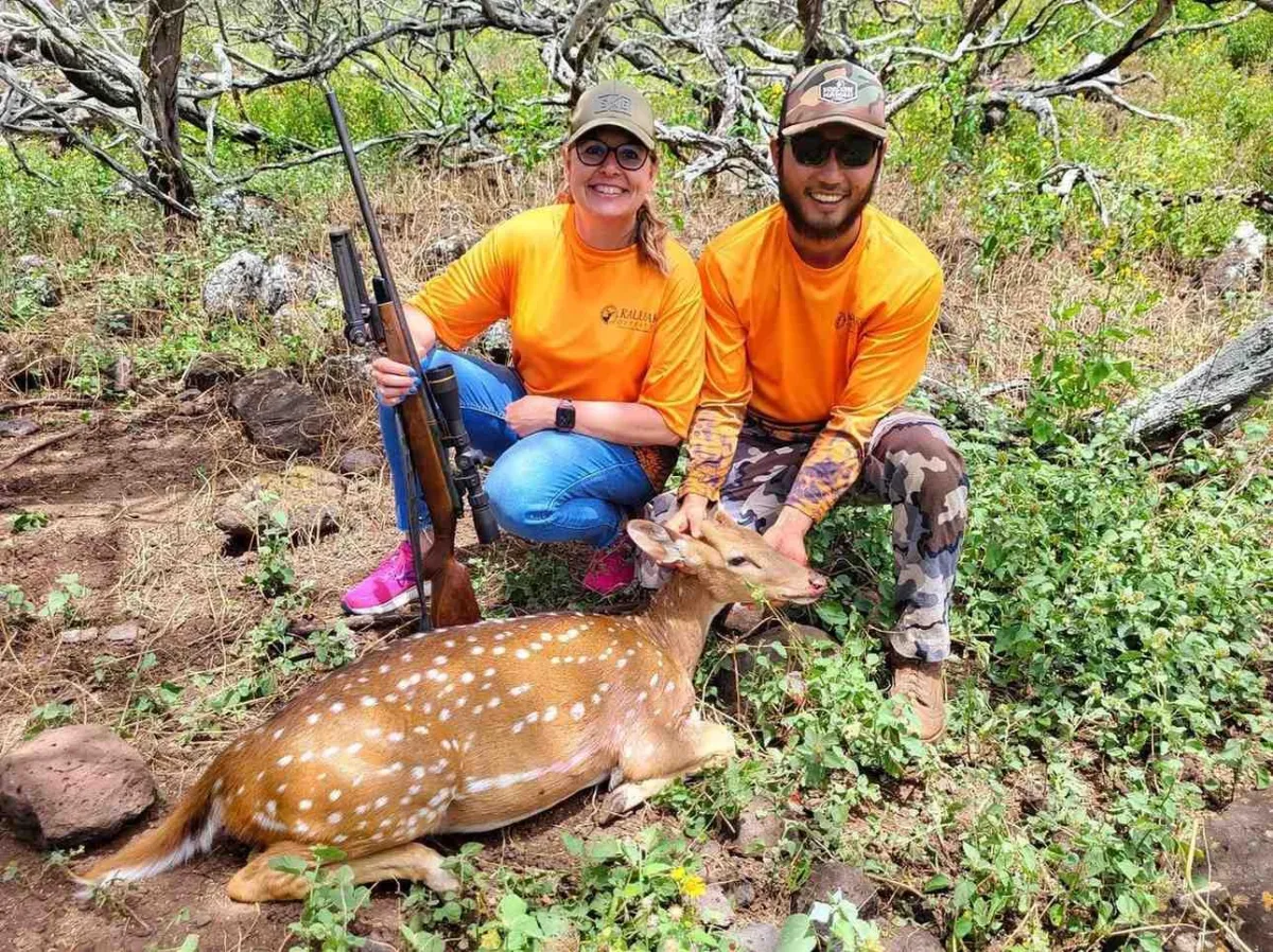 Two hunters standing by an axis deer