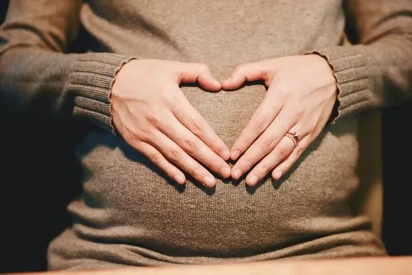 Lady with hands making heart over her pregnant belly.