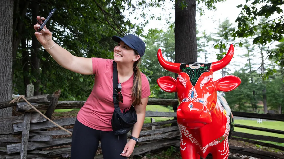 A visitor takes a selfie with a cow designed like a beaded purse