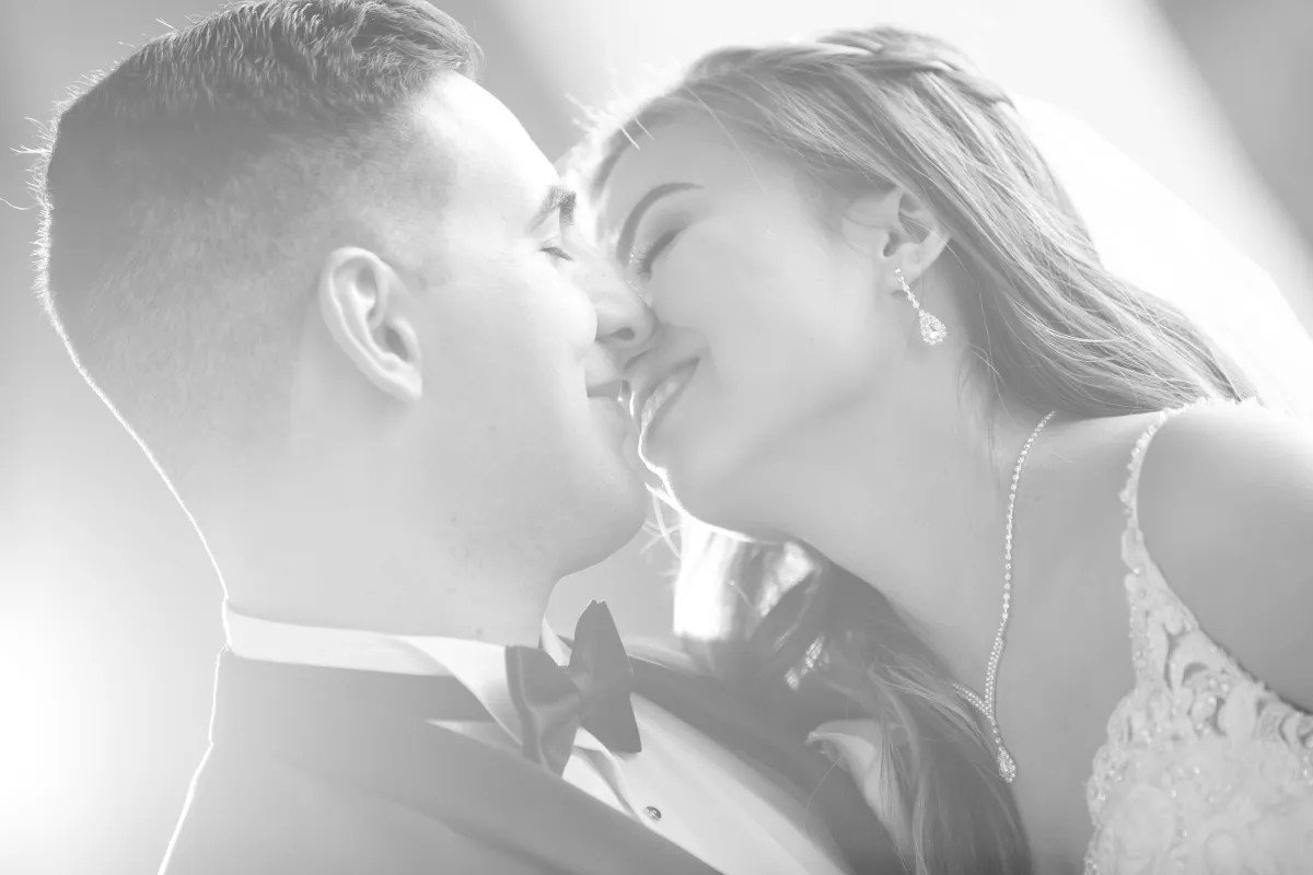 Close-up, black and white portrait of a bride and groom about to kiss, with bright backlighting, showcasing an intimate and joyful moment.
