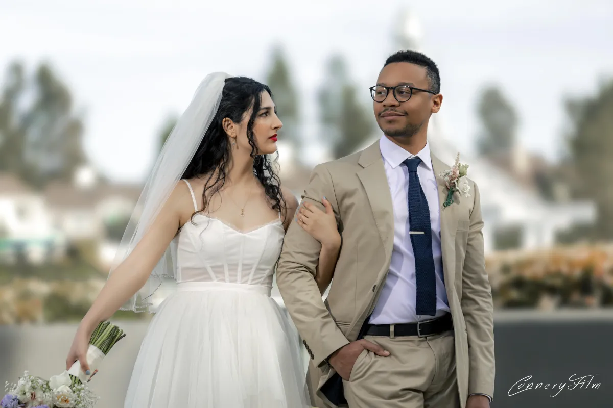 Elegantly dressed bride in a white gown and groom in a beige suit walking arm in arm, symbolizing a sophisticated and joyful wedding day.