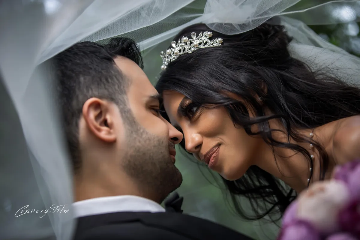 Close-up of a bride and groom looking lovingly at each other under her wedding veil, showcasing an intimate and romantic moment.