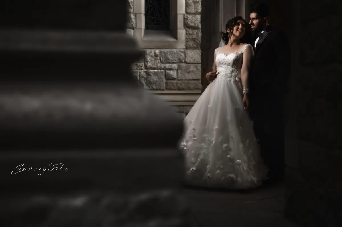 Bride and groom standing together outside a stone chapel, with soft lighting and elegant wedding attire