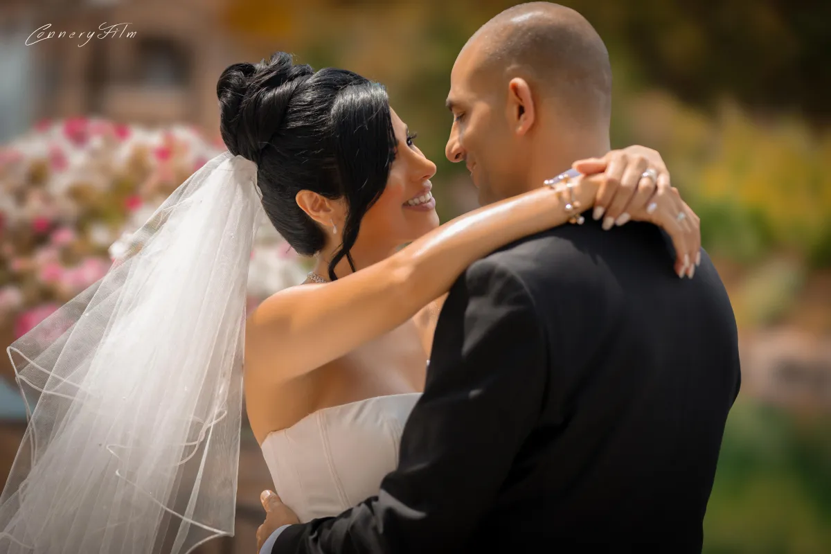 Bride Niki and groom Peyman smiling and embracing during their first dance at their outdoor wedding.