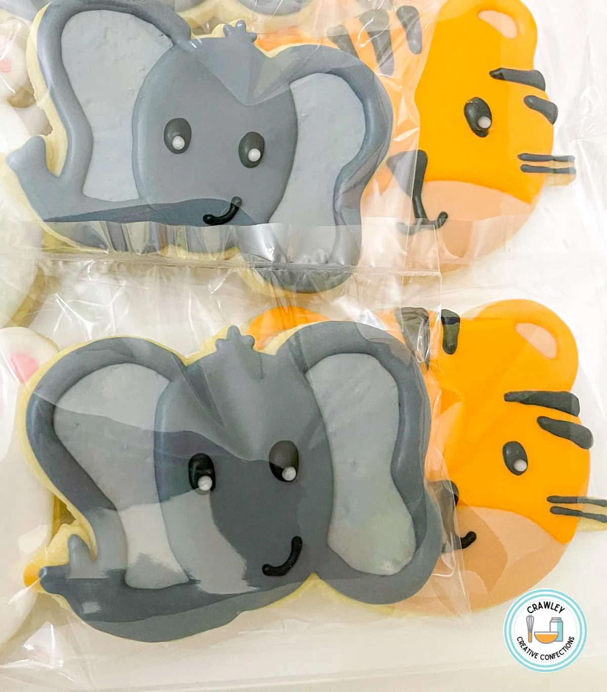 A delightful set of sugar cookies shaped as elephant and tiger faces, each intricately hand-iced with detailed features. The elephant cookies showcase large ears, gentle eyes, and a curved trunk, while the tiger cookies feature bold stripes, expressive eyes, and a friendly smile. The designs capture the charm and personality of these majestic animals.