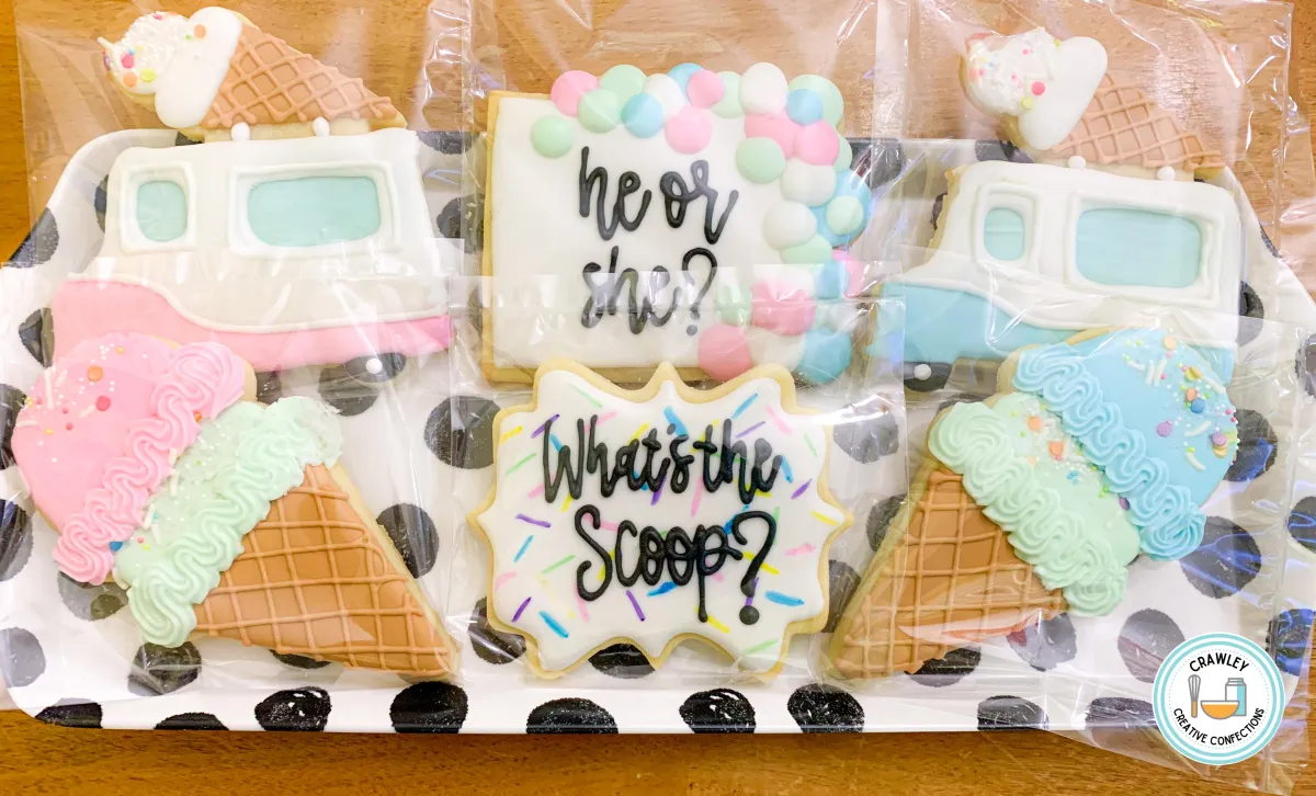 A playful set of sugar cookies for a “What’s the Scoop” gender reveal shower, featuring ice cream trucks, ice cream cones, and pastel sprinkle accents. Each cookie is hand-iced with soft pastel colors and intricate details, creating a sweet and whimsical theme for the celebration.