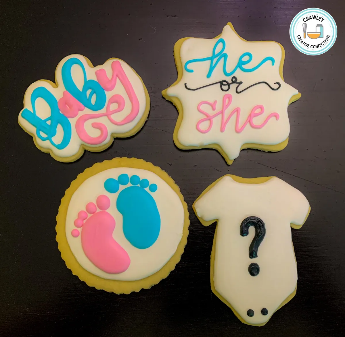 A creative set of sugar cookies for a gender reveal shower featuring pink and blue lettering, tiny baby feet, and onesies with question marks on the front. The onesies hold a surprise—when bitten into, they reveal the baby’s gender with colored icing inside. Each cookie is hand-iced with intricate details, making them both interactive and delightful for the big reveal.