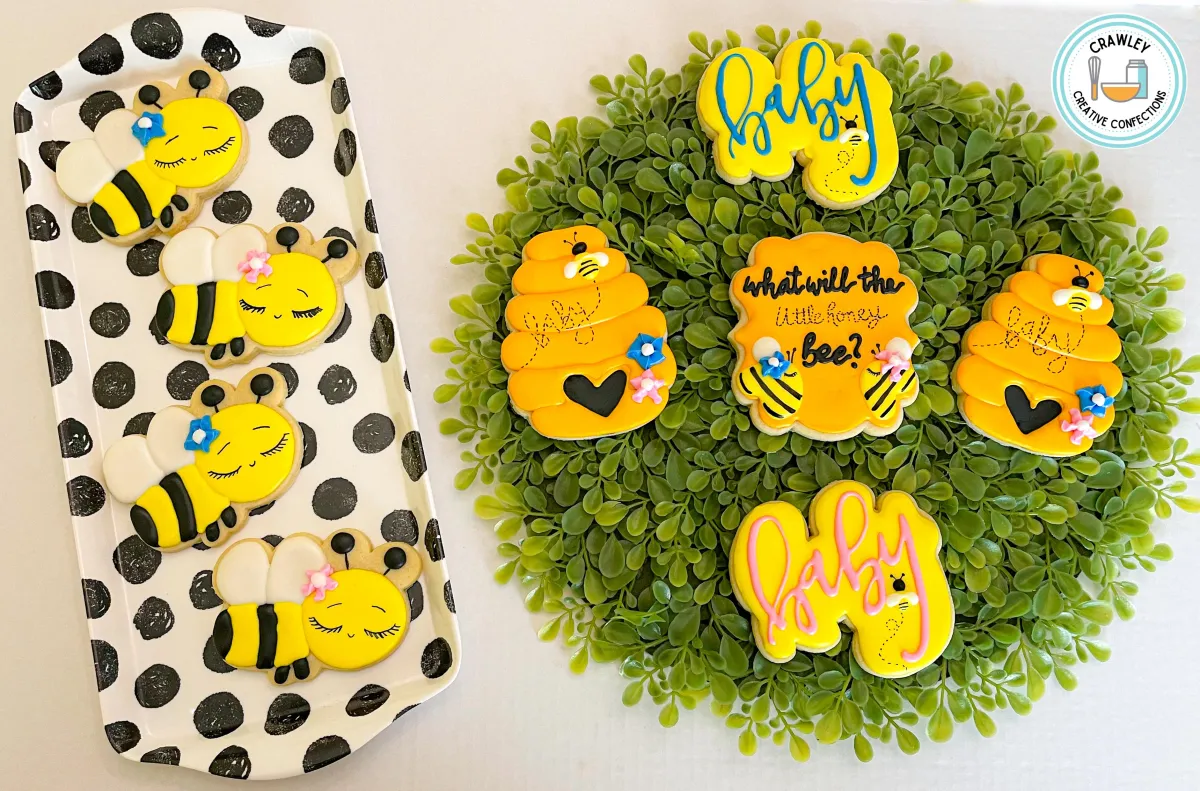 A sweet and whimsical set of sugar cookies for a gender reveal themed “What will he or she ‘bee’?” The designs include honey bee hives, buzzing bumblebee accents, and cookies decorated in blue and pink hues. Each cookie is intricately hand-iced with playful details, creating a charming and fun bee-inspired celebration.