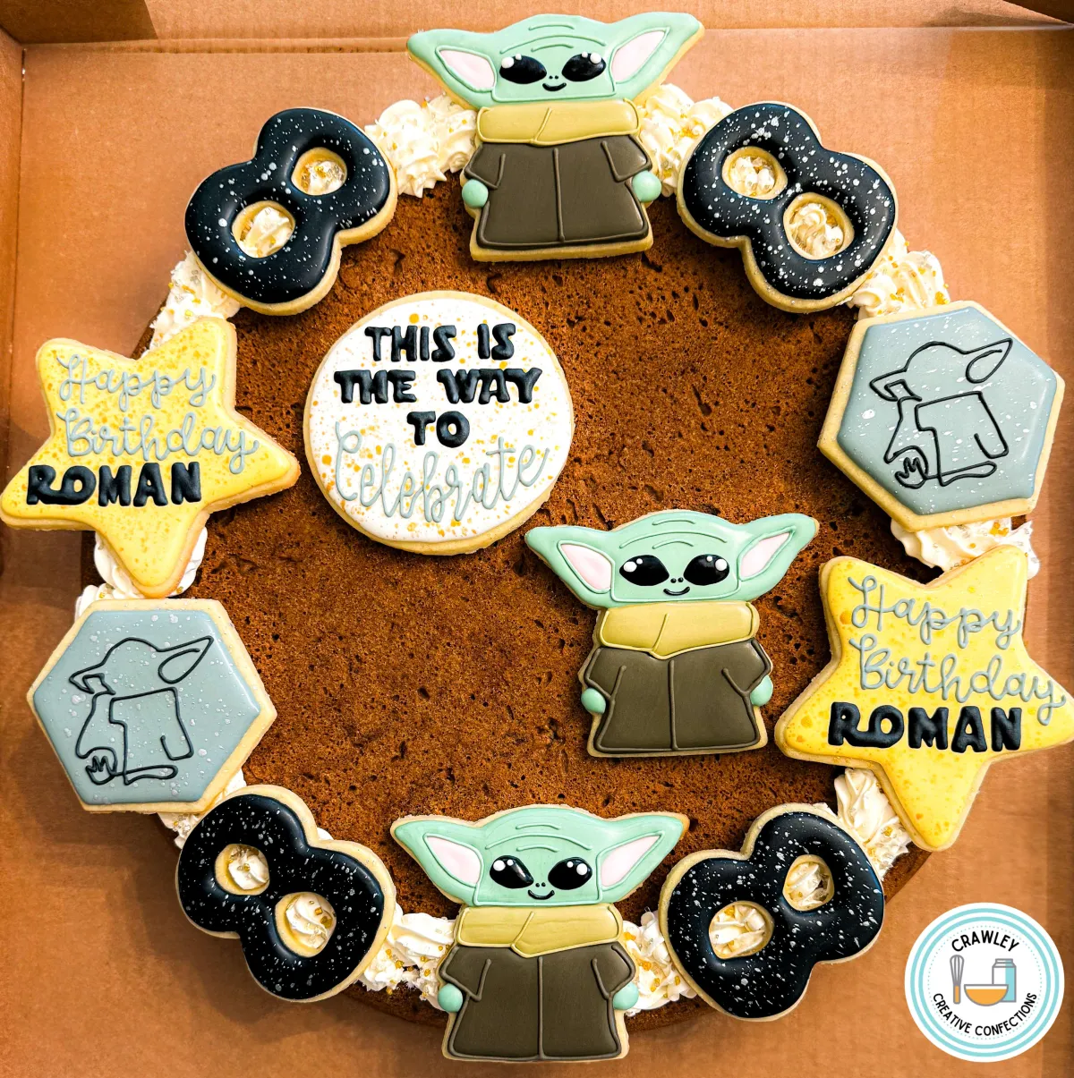 A delicious deep dish cookie cake with chocolate chips, decorated with sugar cookies featuring Baby Yoda and Mandalorian-themed designs for an 8th birthday celebration. The sugar cookies are intricately hand-iced with detailed characters and iconic symbols from the Mandalorian series, creating a fun and personalized dessert for the birthday party.