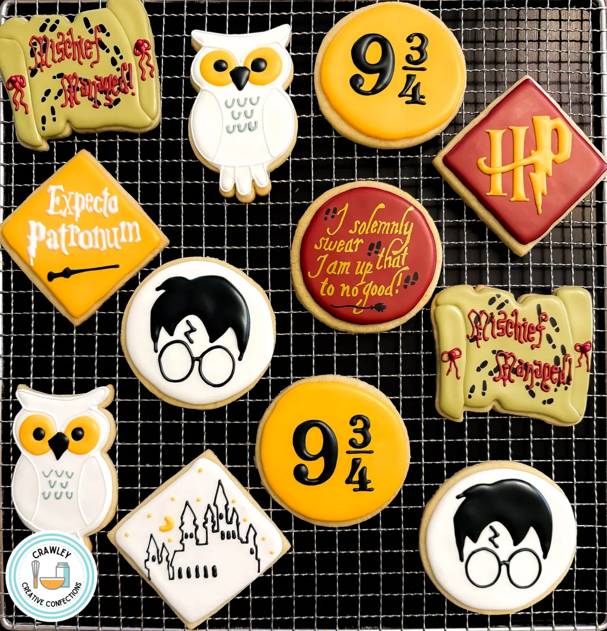 A set of custom wizard-themed sugar cookies displayed on a cooling rack, featuring designs such as the 9 ¾ platform sign, an owl, a lightning-bolt-scarred silhouette, a castle, and magical phrases like “Mischief Managed” and “Expecto Patronum.” The cookies are decorated in gold, red, white, and black, making them perfect for a themed celebration. Created by Crawley Creative Confections.