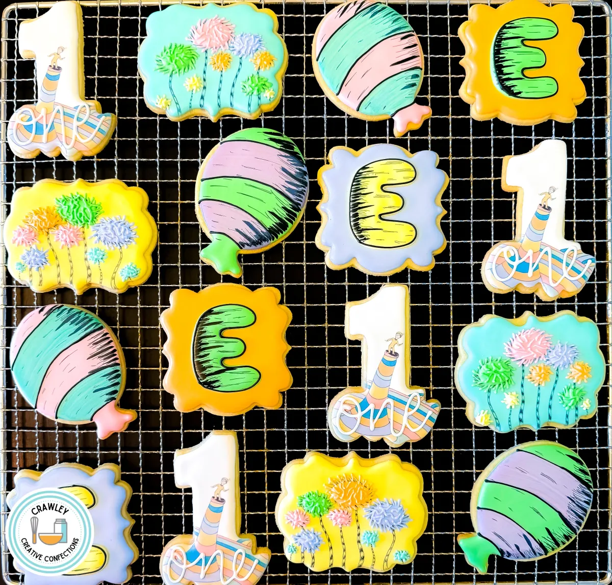 A set of custom Dr. Seuss-inspired first birthday sugar cookies displayed on a cooling rack. The collection features colorful Truffula trees, striped balloons, number “1” cookies, and personalized “E” cookies in bright yellow, green, pink, and blue. Designed for a whimsical first birthday or storybook-themed celebration. Created by Crawley Creative Confections in Louisville, KY.