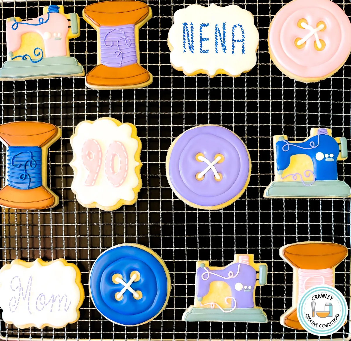 A set of custom sewing-themed sugar cookies displayed on a cooling rack. The collection includes cookies shaped like vintage sewing machines, thread spools, and buttons, along with personalized name and age plaques in pastel shades of pink, blue, purple, and white. Designed for a sewing enthusiast’s birthday, Mother’s Day, or a crafting-themed celebration. Created by Crawley Creative Confections in Louisville, KY.