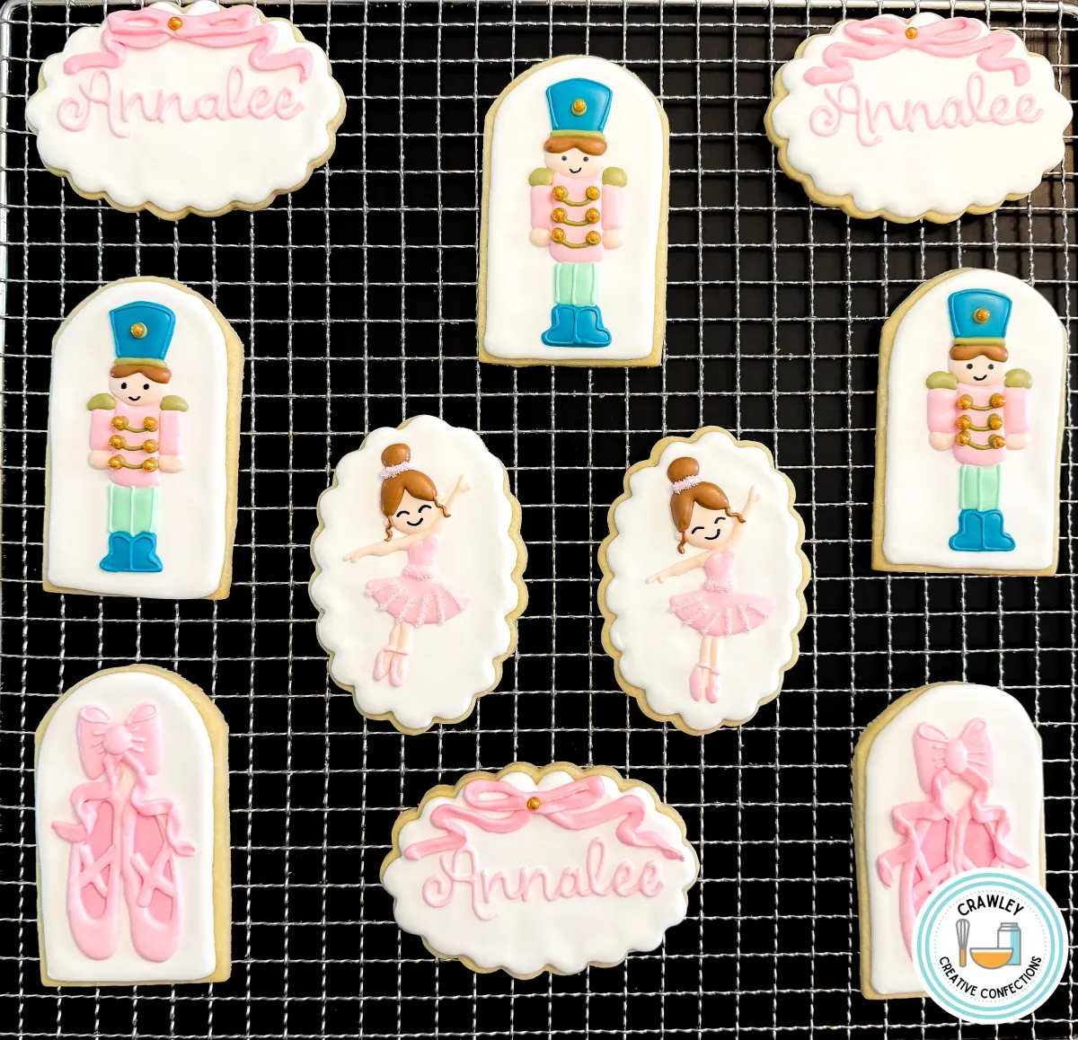 A set of custom Nutcracker ballet-themed sugar cookies displayed on a cooling rack. The collection includes ballerinas in pink tutus, toy soldier cookies, ballet slippers, and personalized name plaques with “Annalee.” Decorated in soft pink, white, and gold details, these cookies are perfect for dance recitals, ballet-themed birthdays, or Nutcracker performances. Created by Crawley Creative Confections in Louisville, KY.