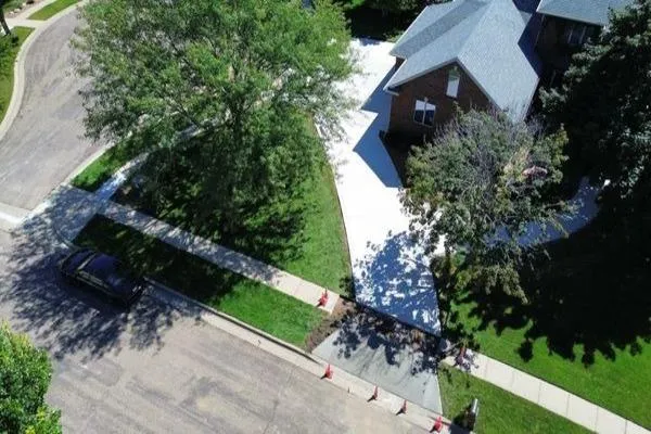 Aerial view of a residential neighborhood featuring a driveway and a parked car amidst houses and greenery.