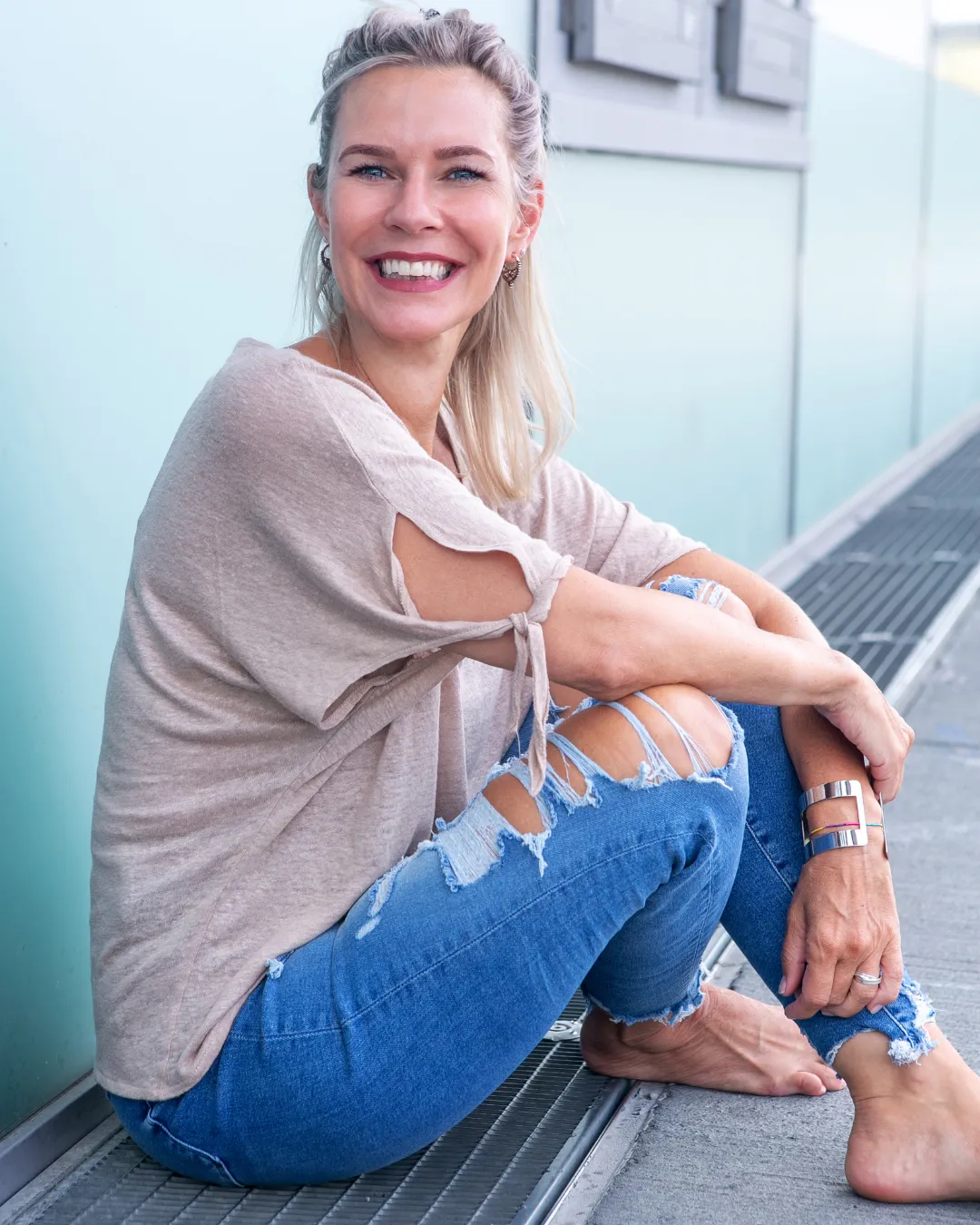 Confident midlife woman in a white T-shirt and torn jeans sitting in natural light, radiating freedom, strength, and body wisdom through menopause recalibration.
