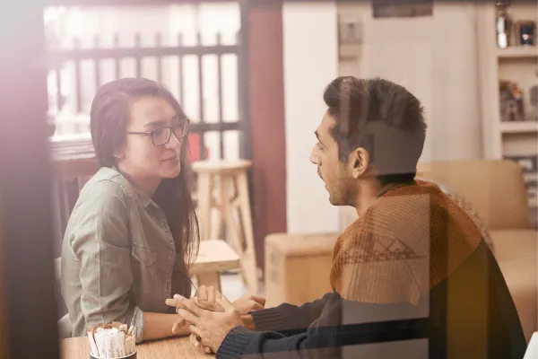 A man and a woman sitting across each other at a table talking