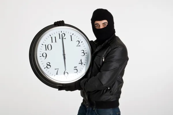 This image depicts a person dressed as a thief, wearing a black mask and leather jacket, holding a large wall clock. The visual humorously conveys the concept of "stealing time" and could represent themes such as procrastination, time management, or metaphorical concepts like feeling as though time is being taken away.
