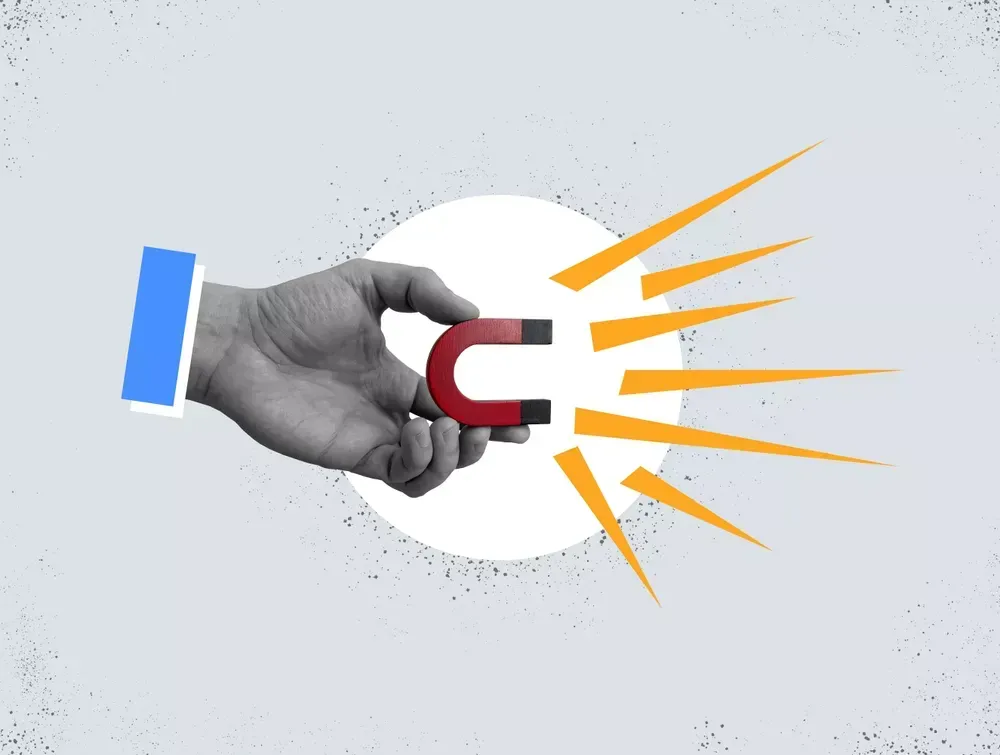 A hand holding a red and black horseshoe magnet, illustrated with yellow lines representing magnetic force, against a light gray background—perfectly capturing the essence of lead generation in sales & marketing automation.