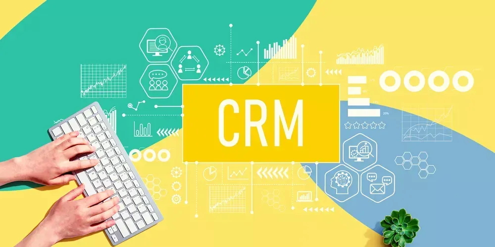 Hands typing on a keyboard with a colorful background displaying "CRM" and various data visualizations, highlighting the seamless integration of automation in customer relationship management.