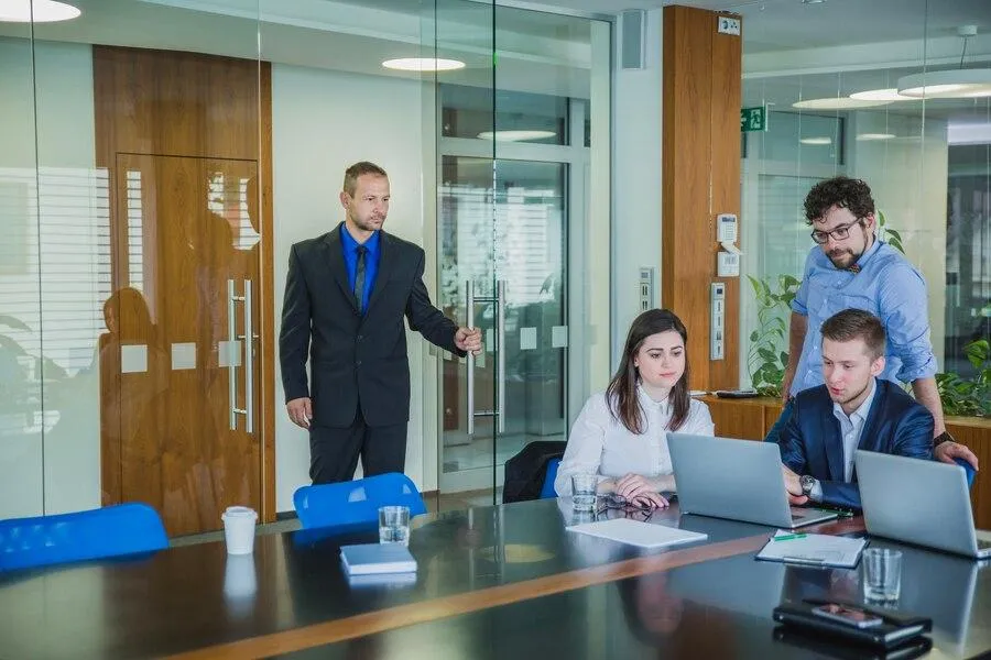 A man confidently strides into a well-lit office room, greeted by smiling coworkers / recruiters