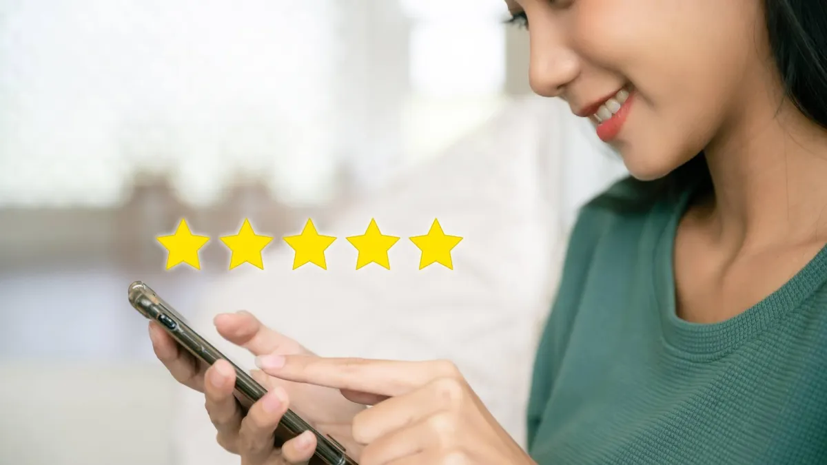 A person smiles while looking at their phone, and there are five yellow stars up on the screen, demonstrating a customer review collection system.