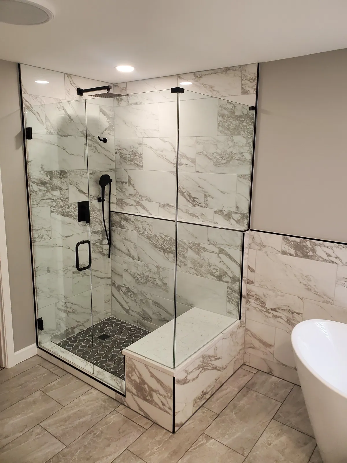 Frameless glass shower with marble tile and bench installed by RDB Glass in Springboro OH