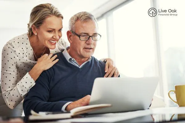 Happy couple in their early 60s sitting together and smiling while looking at a laptop, symbolizing confident and informed retirement planning.