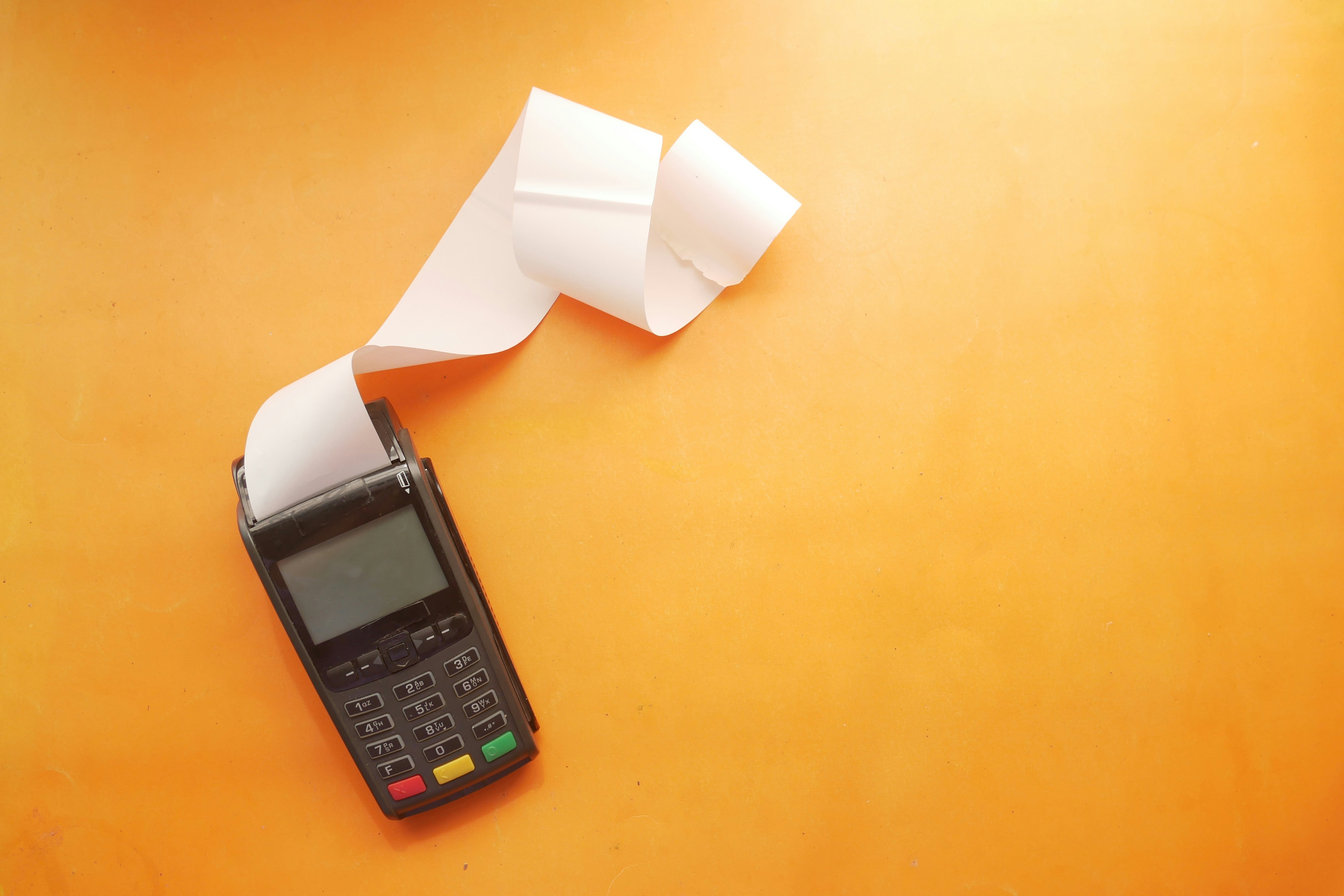 Credit card payment terminal printing a long receipt on an orange background