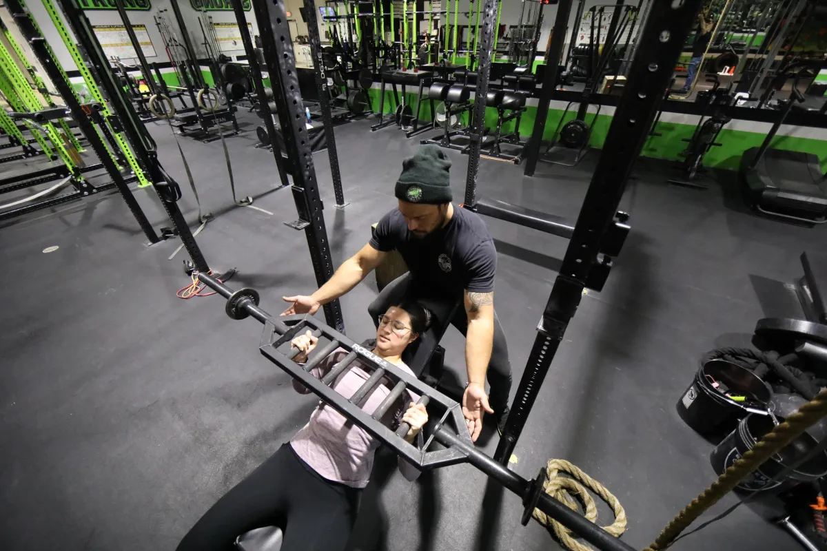 A personal trainer giving assistance on a bench press for a client.