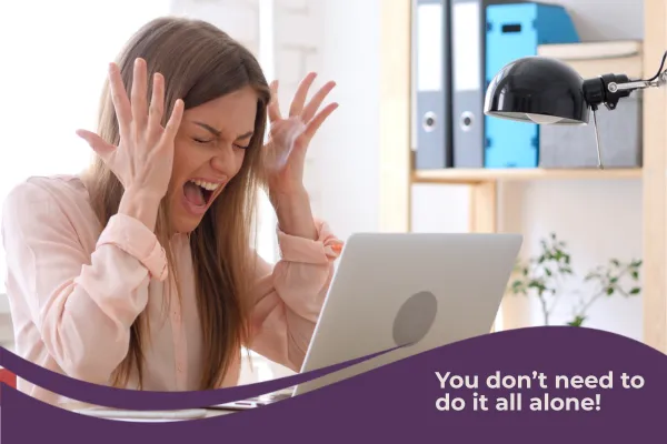 Frustrated woman with her hands by her head, sitting in front of a laptop, with text saying “You don’t need to do it all alone”