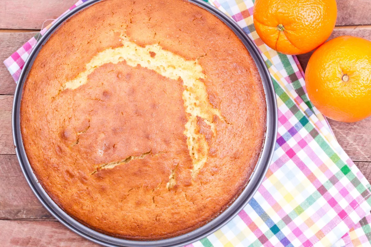 Orange Cake in cake pan with oranges on a tablecloth