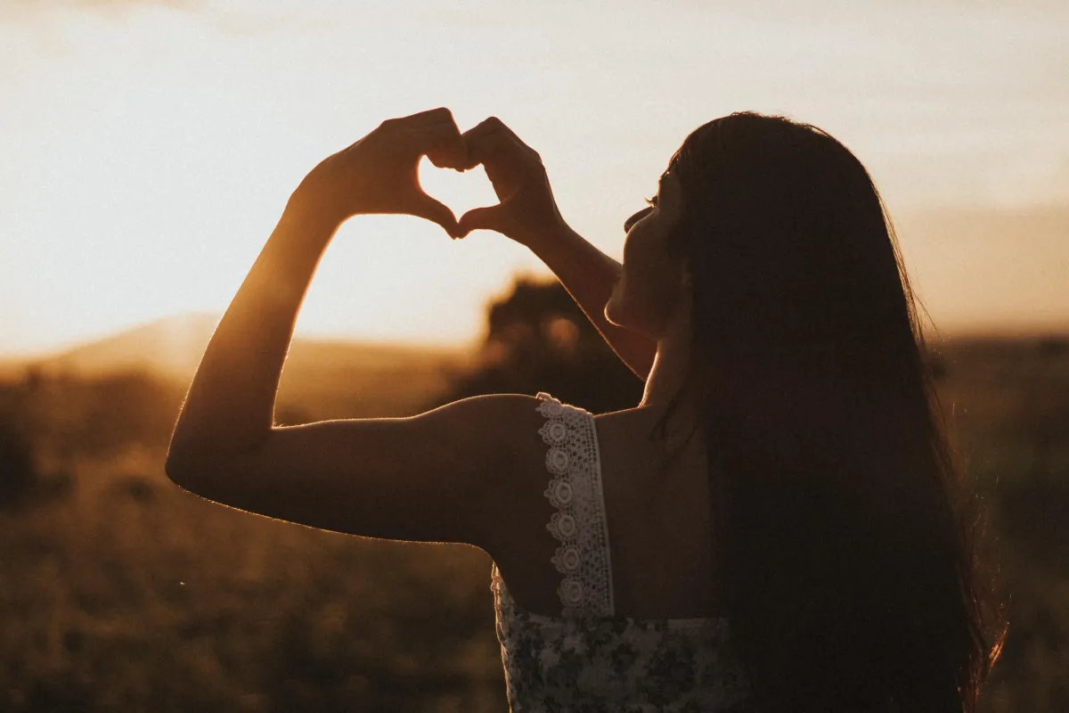 Woman making a heart shape with her fingers against the sun, depicting self-love or self-care