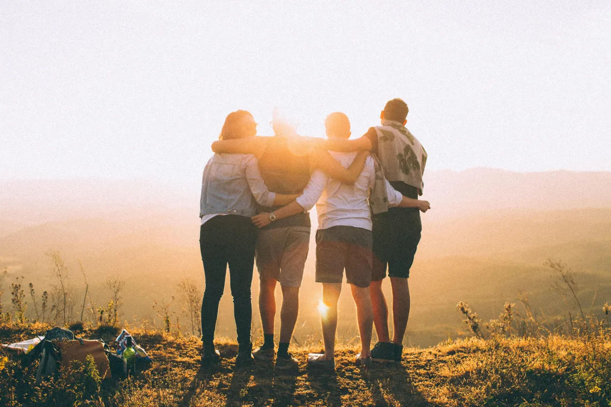 A family of 4 embracing as they look out into the sun from a viewpoint, suggesting an achievement together