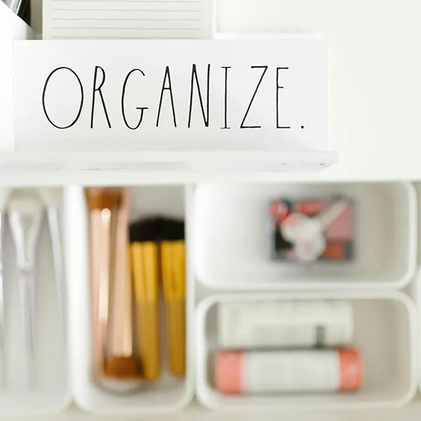 An organized drawer with labelled “Organize” and containing compartments for makeup brushes, cosmetics, and sunglasses.