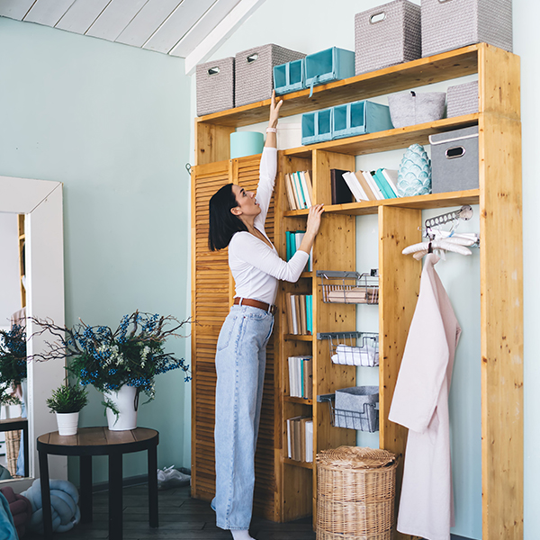 Woman reaching for an item on a high shelf in a well-organized wooden closet.