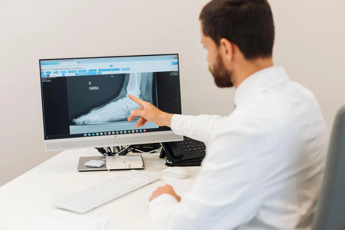 Médico ortopedista do Ortocentro a explicar radiografia do tornozelo a um paciente durante consulta.