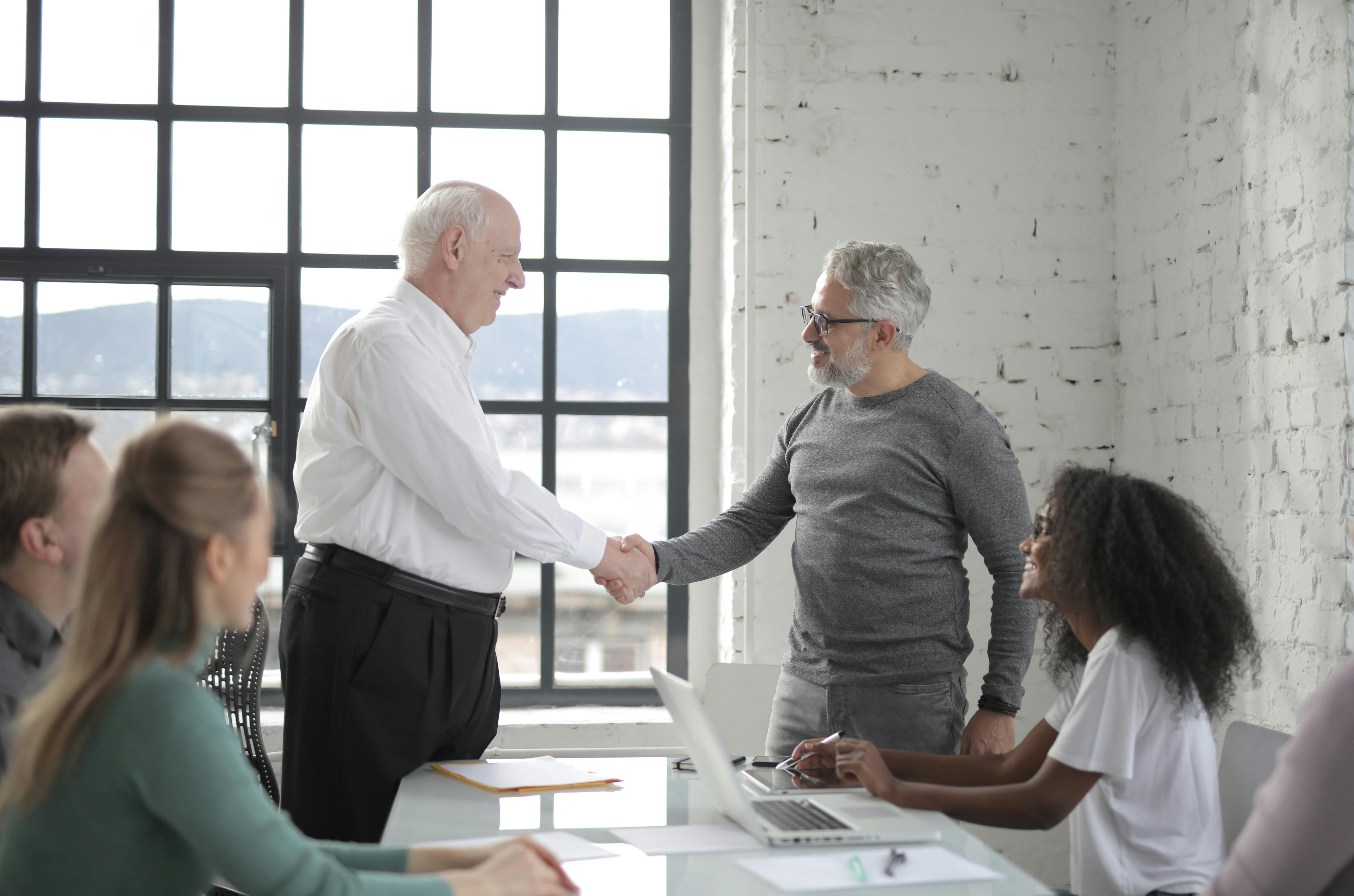 Cheerful different ages colleagues shacking hands in office