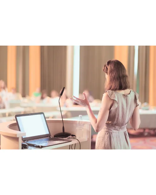 Woman with microphone speaking to an audience at a conference podium.