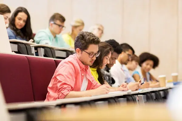 Students sitting in a lecture hall, focused on taking notes during a class