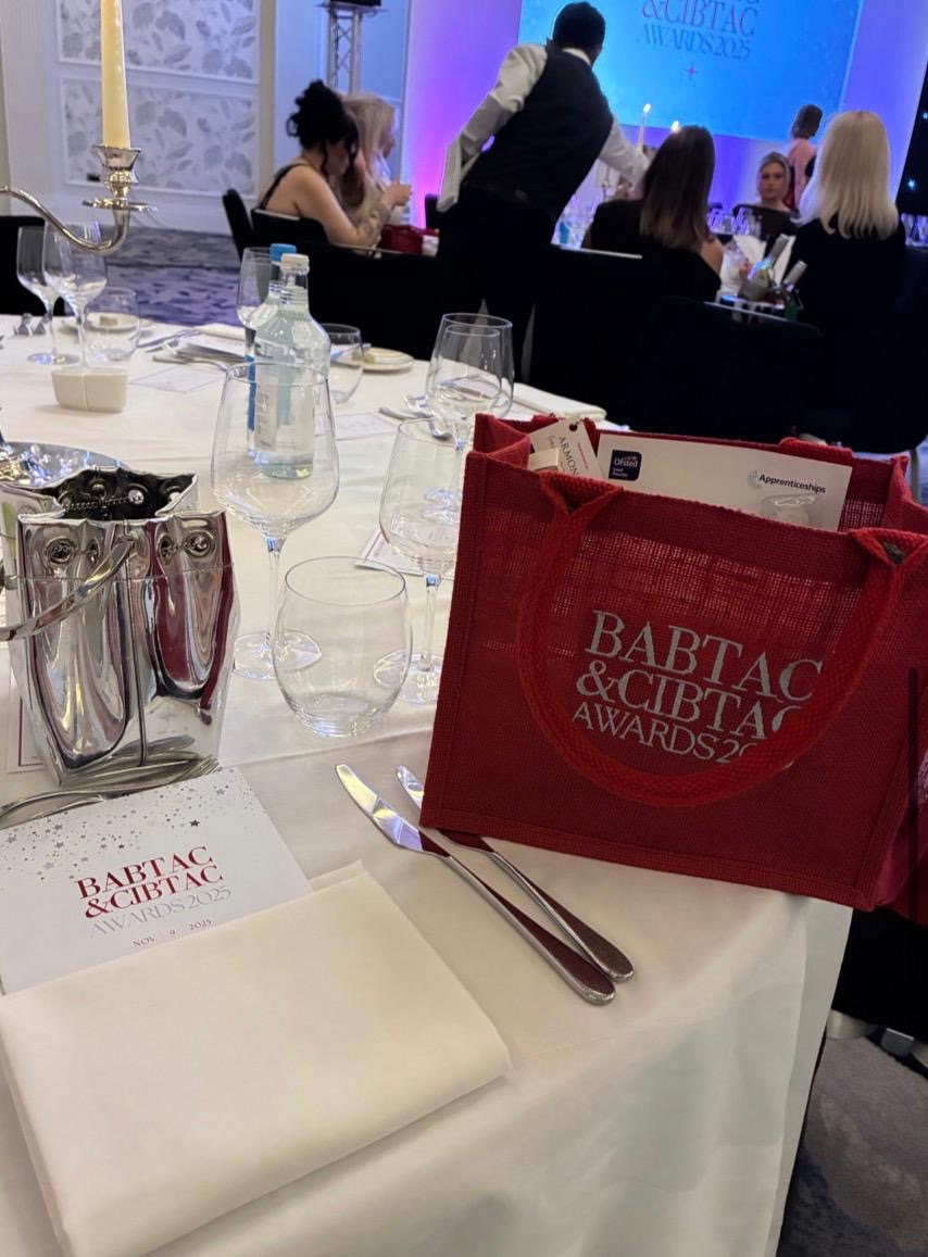 Table setting at the BABTAC & CIBTAC Beauty Awards 2025 held at Fairmont Windsor, showing branded awards tote bags, programmes, glassware, and the stage in the background.