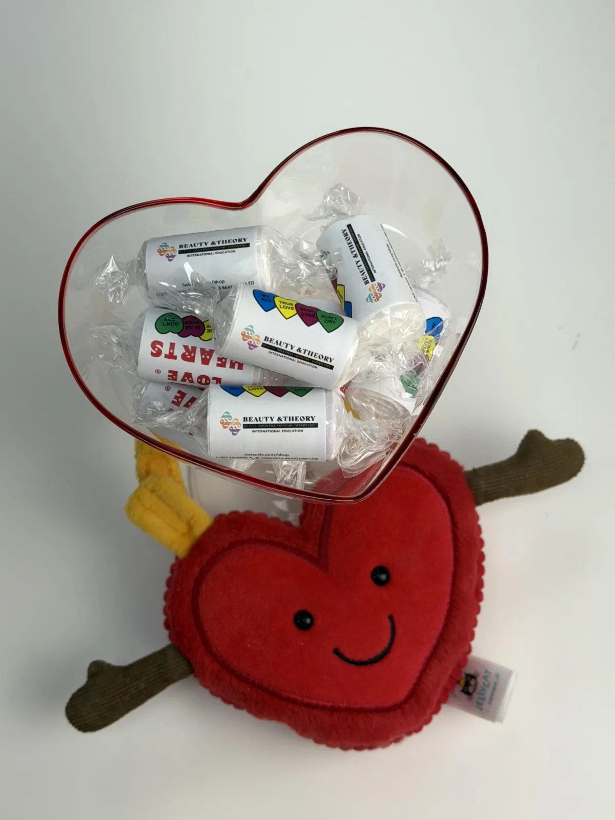 a love heart jellycat locked onto a love heart martini glass with multiple loeheart sweets with 'beauty and theory' logo branding