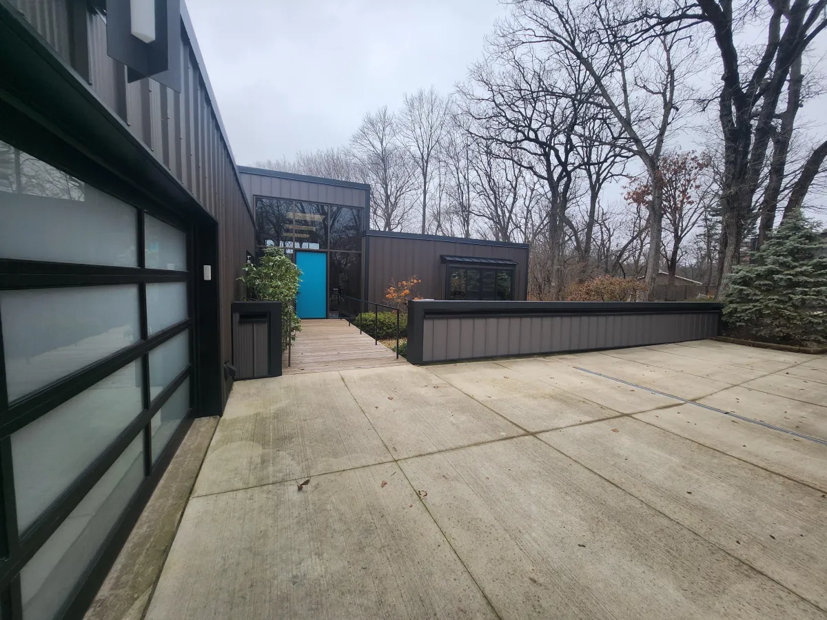 Modern home exterior remodel by M.G.K. Contracting in Rockford IL – glass garage door, custom front entry door with transom and sidelight windows, steel siding