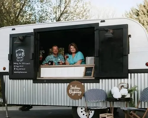 The Keg and Barrel Mobile Bar owners smiling inside their mobile bar trailer, ready to serve the event with signature cocktails. 