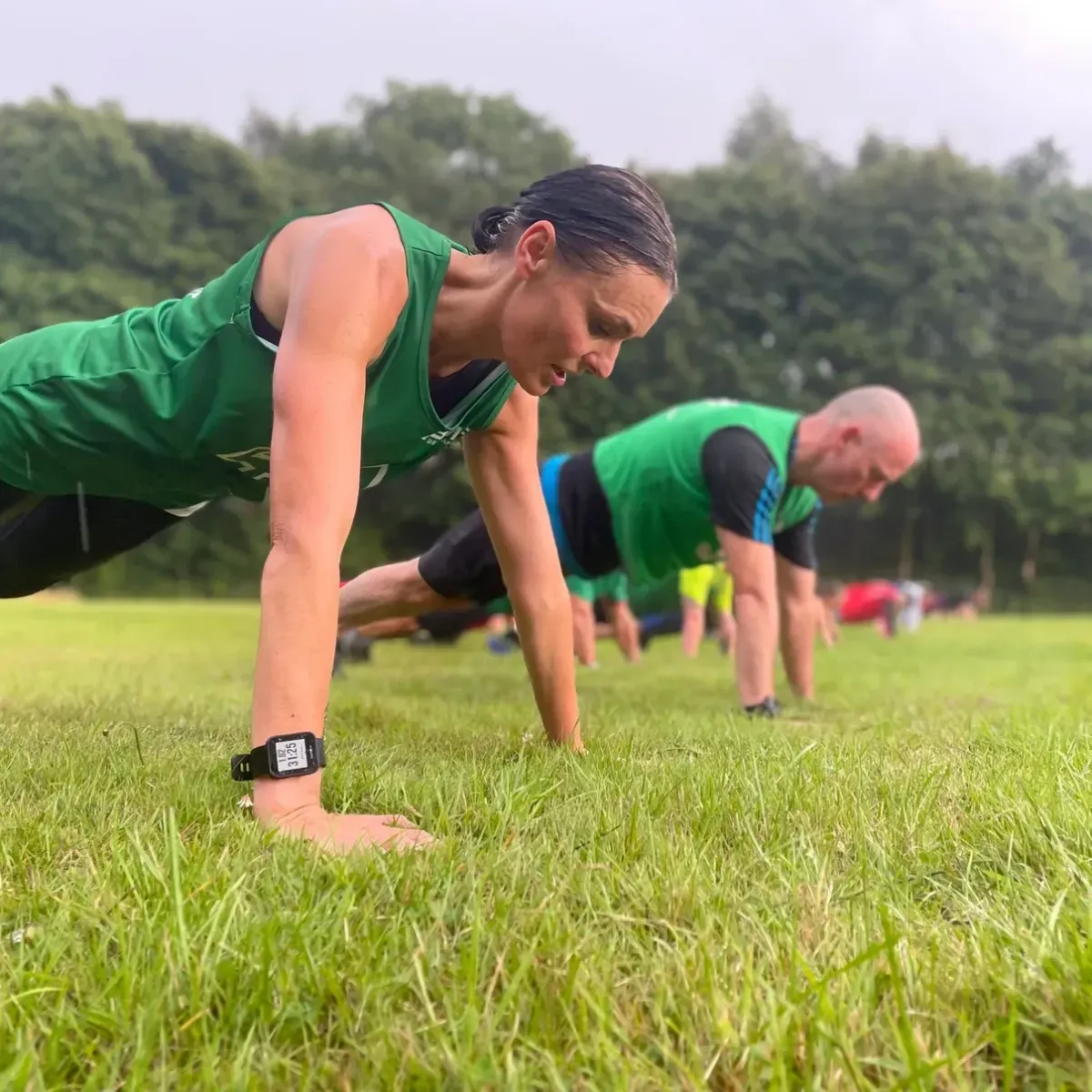 Manchester Outdoor Fitness members doing push-ups on grass during a group training session outdoors.