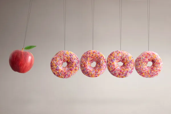 One apple dangles next to four hanging donuts – imagery represents a difference between marketing and advertising.
