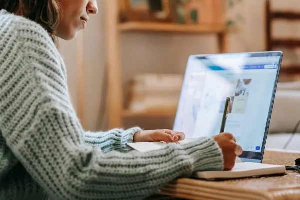 Woman in a light sage knitted sweater writing in front of her computer – represents the importance of creating a content strategy.