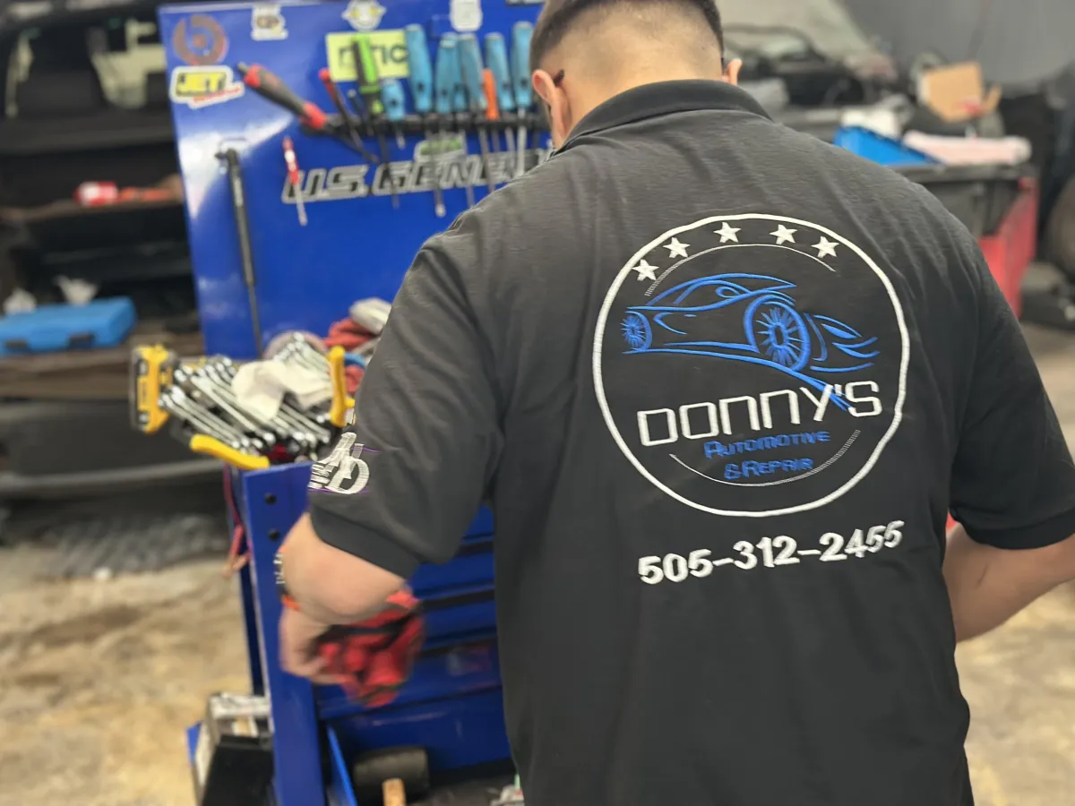 "A mechanic at Donny's Automotive LLC wearing a branded shirt with the shop's logo and contact number, working at a well-organized tool station filled with professional equipment. The image highlights the expertise and professionalism of the team."