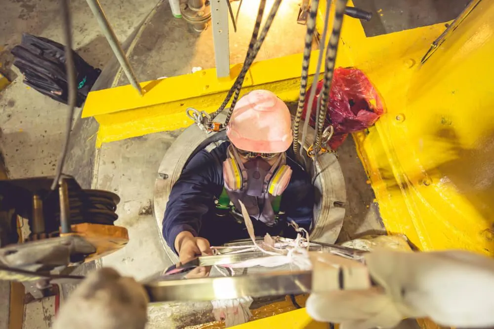 A worker, wearing helmet and harness going inside a confined space