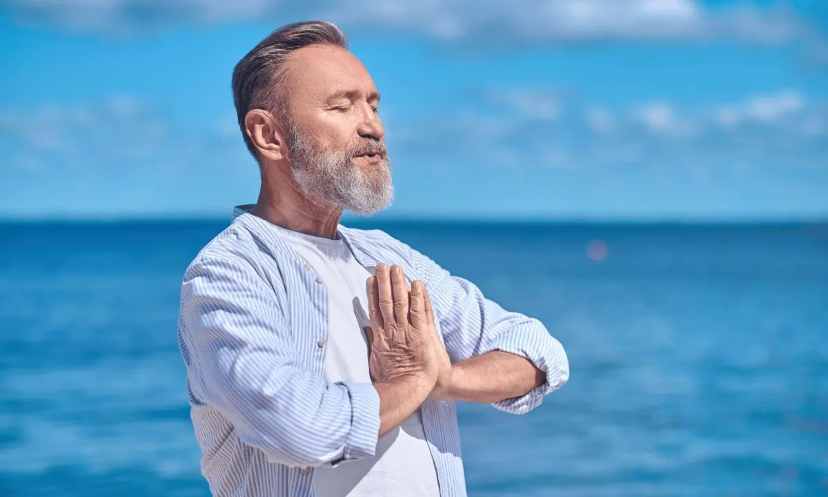 Person standing near water mediating under a clear blue sky.