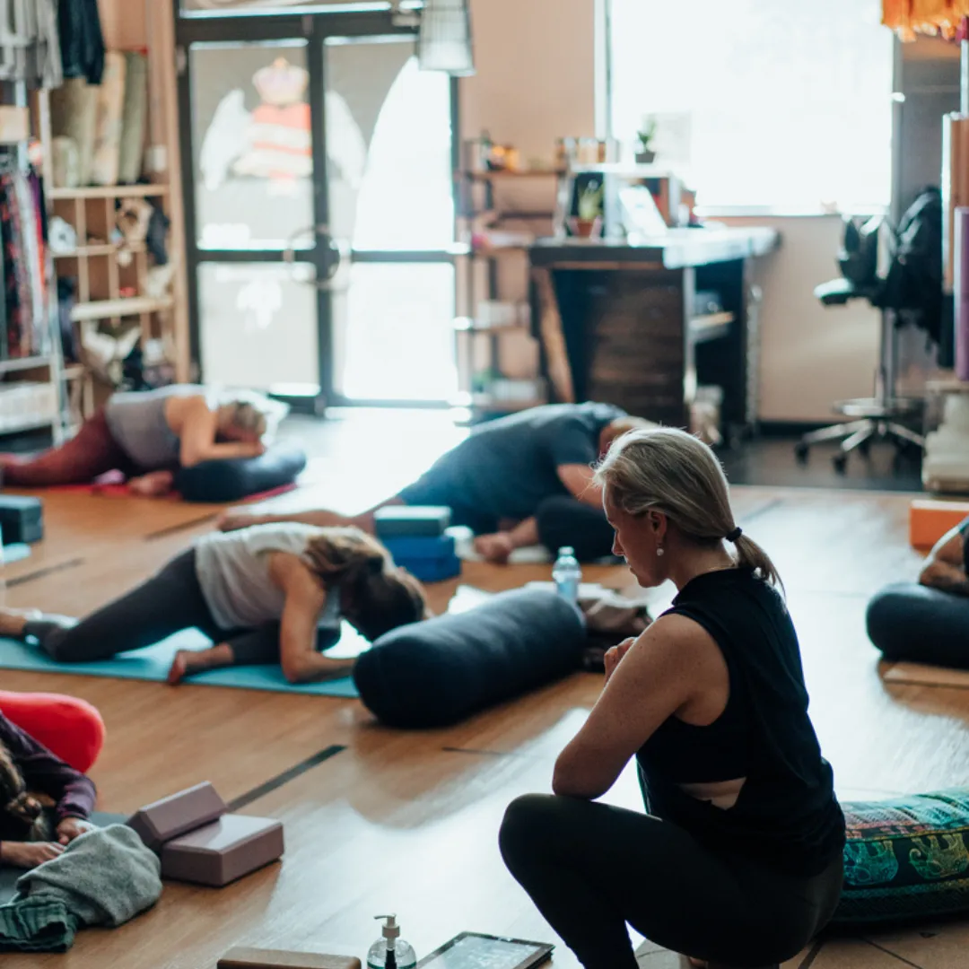 Person practising Half Shoulder Stand yoga pose on a mat with hands supporting lower back, legs extended upward, in a calm indoor yoga studio setting.